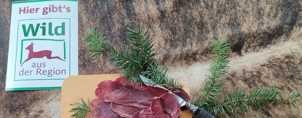 Wildbret Vermarktung – Brett mit Fleisch, einem Jagdmesser und Zweigen, liegen auf einem Fell